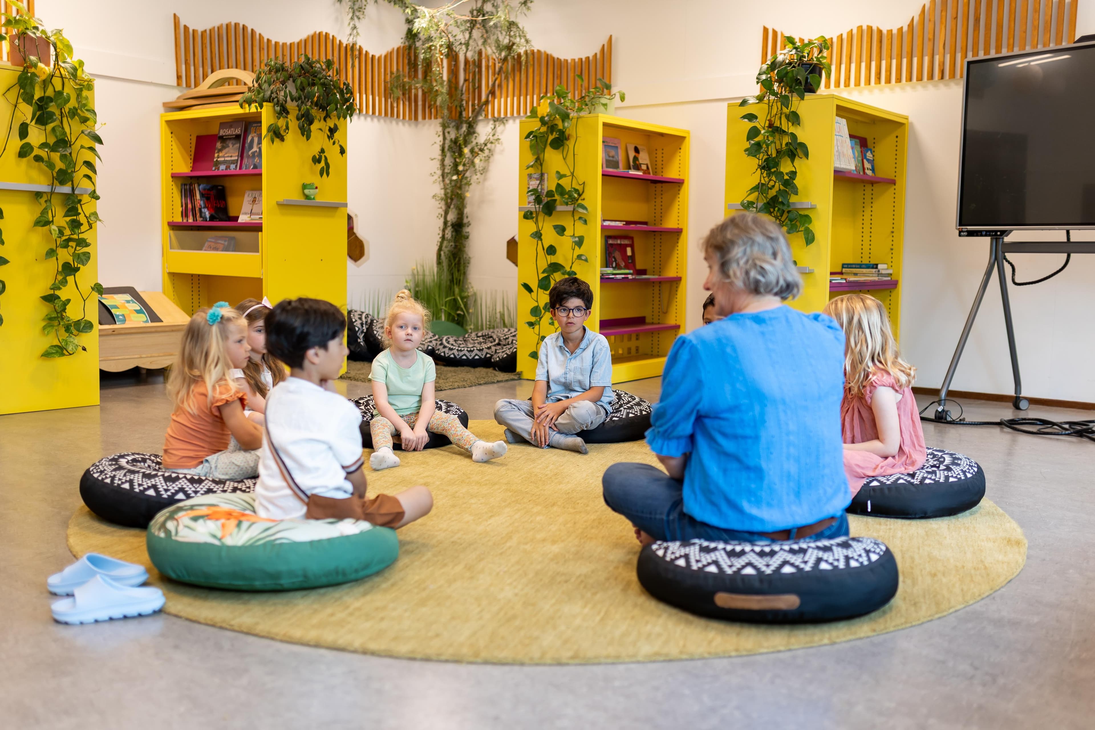 Basisschool De Cirkel, School van Vrede Almere: kinderen en juf in cirkelwerking op de gele vloerkleed in de leesruimte